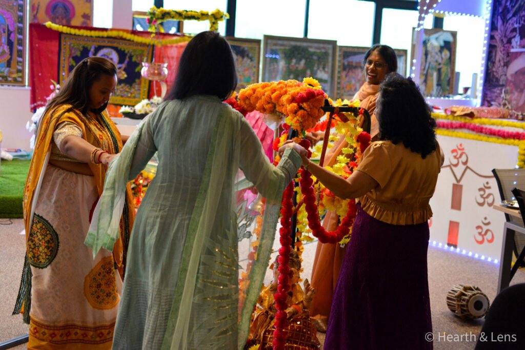 Women dancing together around the decorated jhula during the Janmashtami celebration at Dharma Mandir Newport.